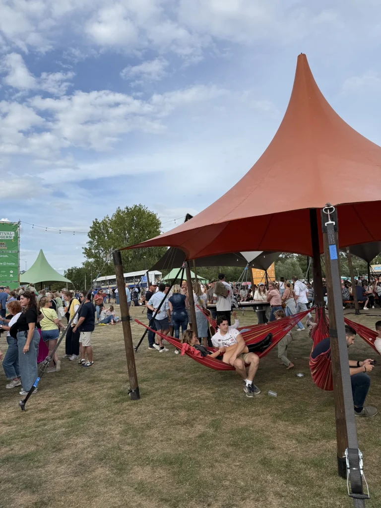Hangmatten onder een rode schaduwtent tussen festivalgangers op Fairway Festival 2025