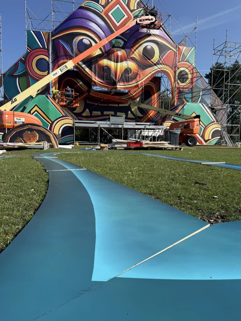 Magic Island 2025 main stage under construction with an aerial lift and blue walkway